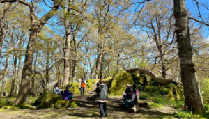 A group of people sit in a forest writing and discussing literature