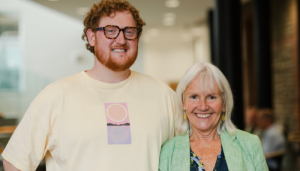 A man with ginger hair and a woman with white hair smile at the camera.